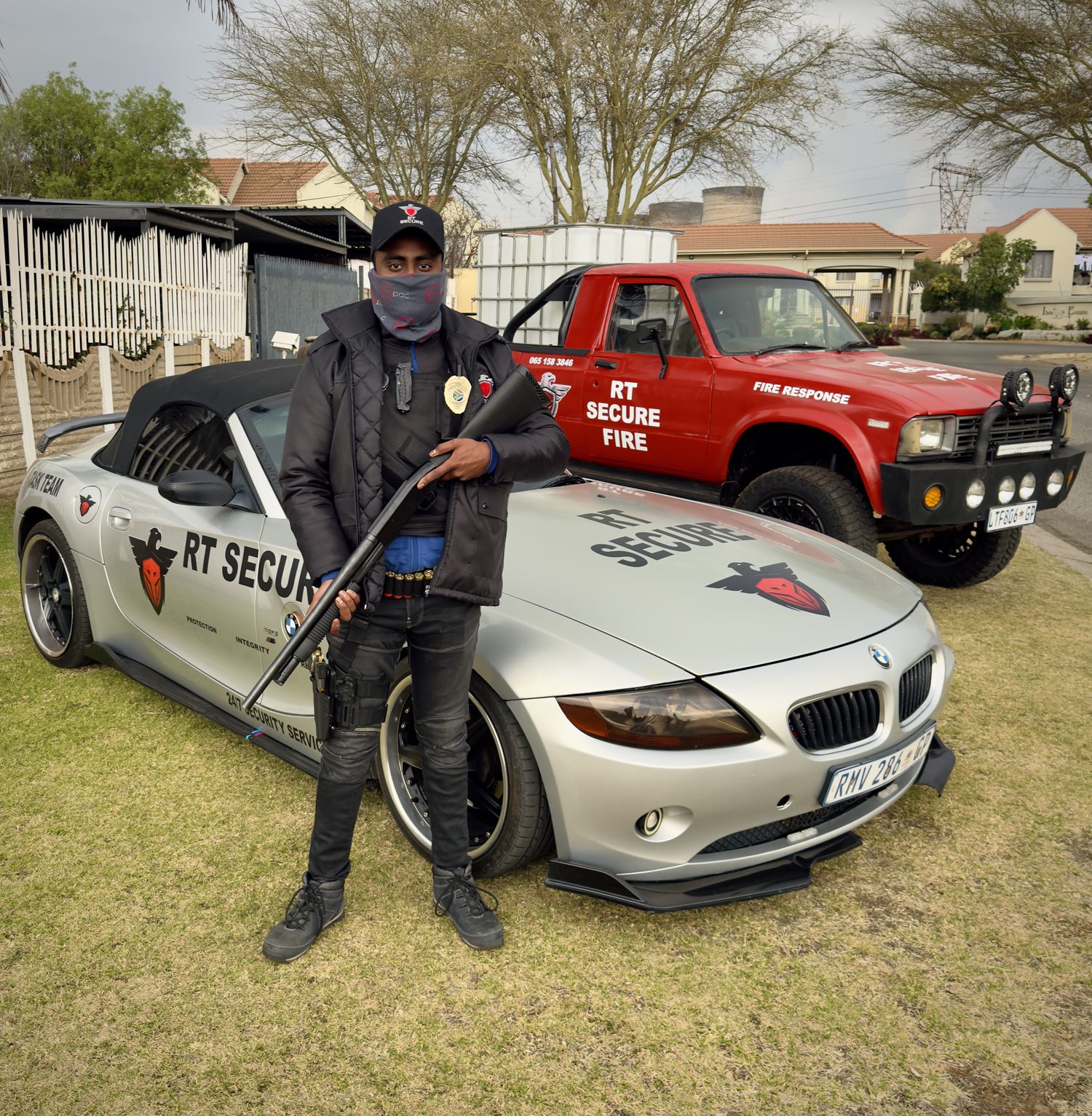 An RT Secure armed response officer standing with the task team vehicle and the fire response bakkie